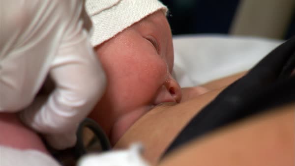 Close-up face of baby sucking at mother's nipple; nurse checking baby with stethoscope - Stock Video Footage - Dissolve