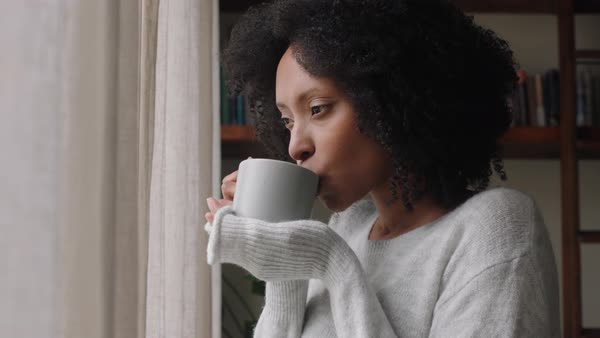 Beautiful african american woman looking out window drinking coffee