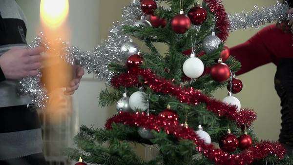 Young Romantic Couple Decorating Christmas Tree By A Fireplace
