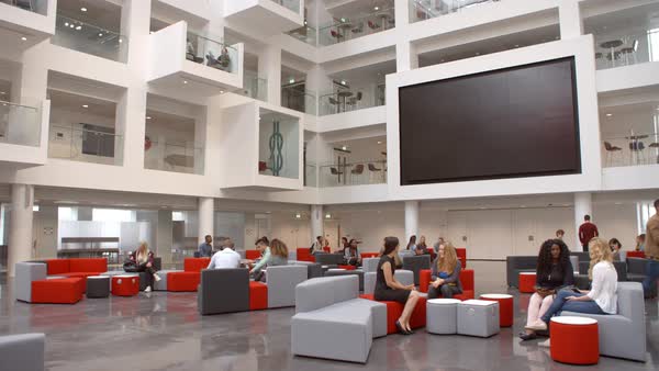 Students sit talking under AV screen in atrium at university - Stock ... Students sit talking under AV screen in atrium at university - Stock ...