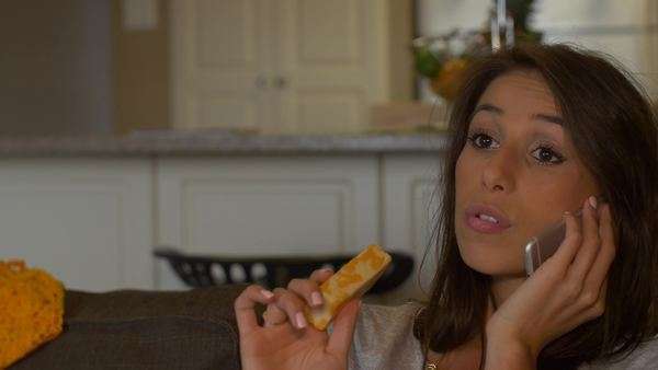 Attractive Woman Eats Cheese Talking On Phone On A Couch Stock