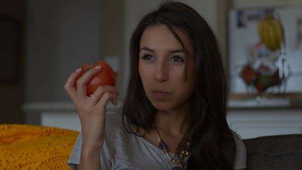 Attractive Woman On Couch Eats Big Red Tomato While Watching Tv