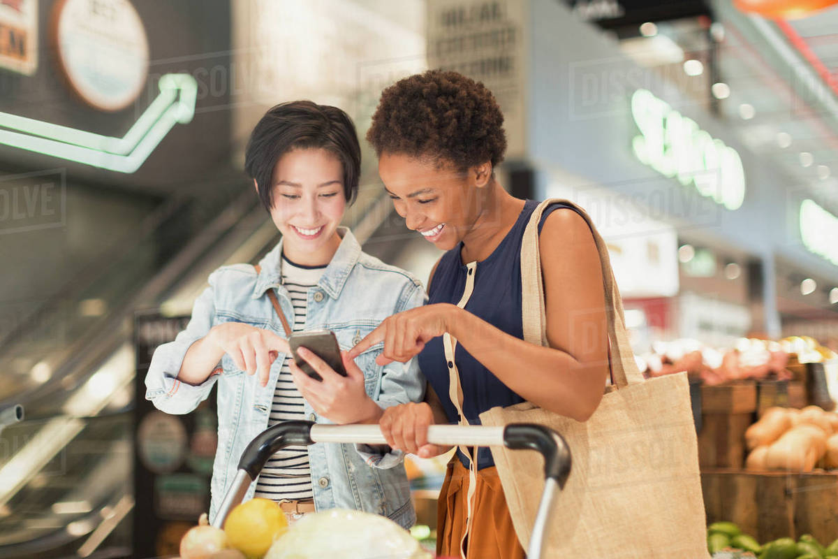 Young lesbian couple using cell phone, grocery shopping in market Royalty-free stock photo