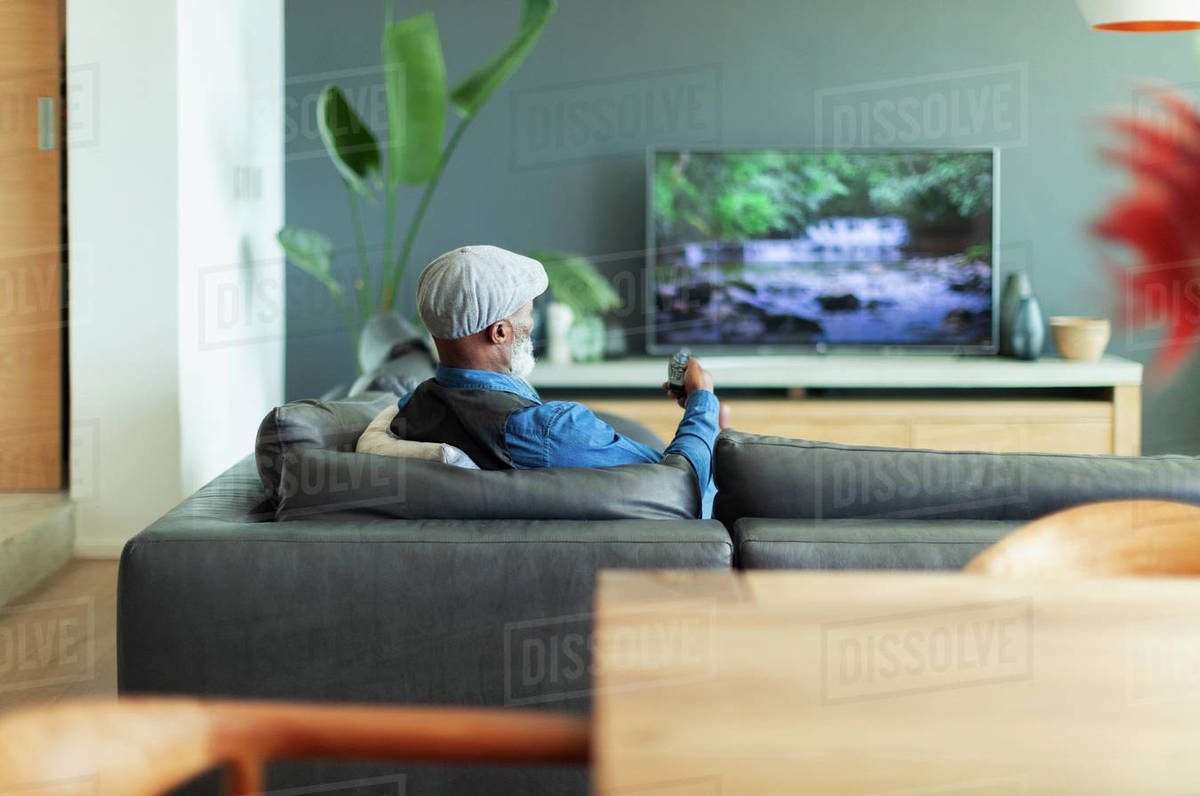 Man watching TV on living room sofa Stock Photo Dissolve