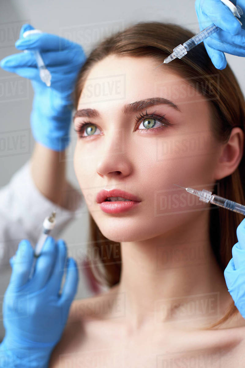 Hands of beauticians holding syringes around doll like woman face ready