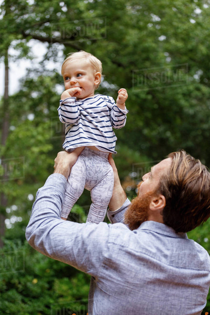 Father holding baby girl in air, outdoors Stock Photo Dissolve