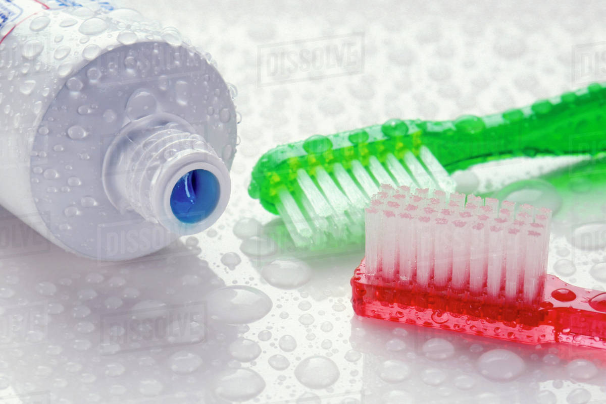 Closeup of toothpaste and toothbrushes covered with water drops