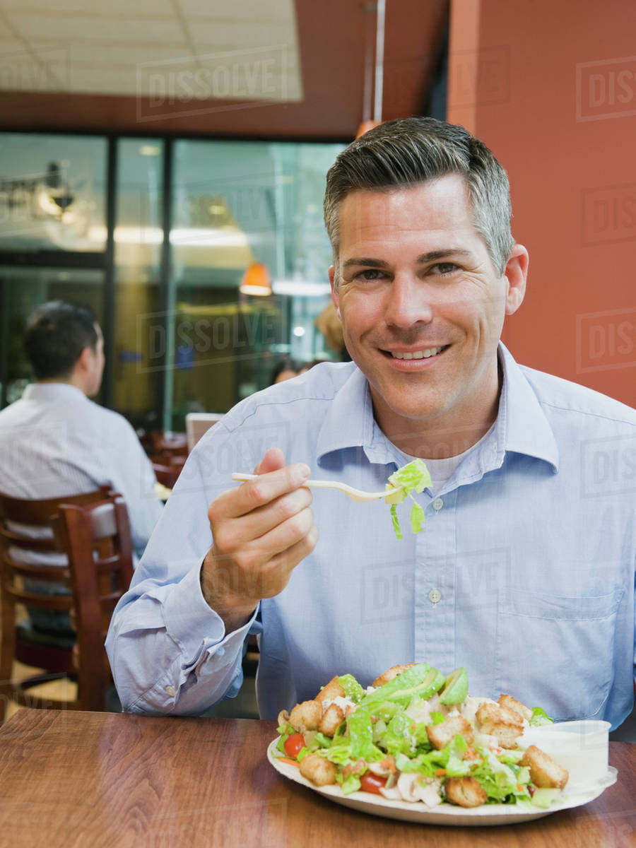 Man eating salad in restaurant Stock Photo Dissolve