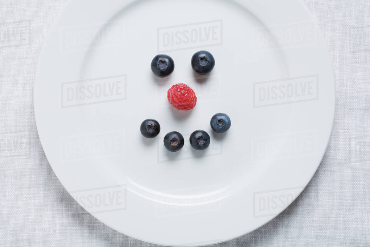 Smiley face of blueberries and raspberry on white plate - Royalty-free ...