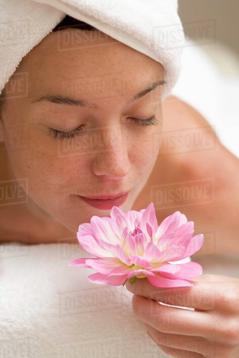 Woman lying on white towel, smelling flower Stock Photo Dissolve