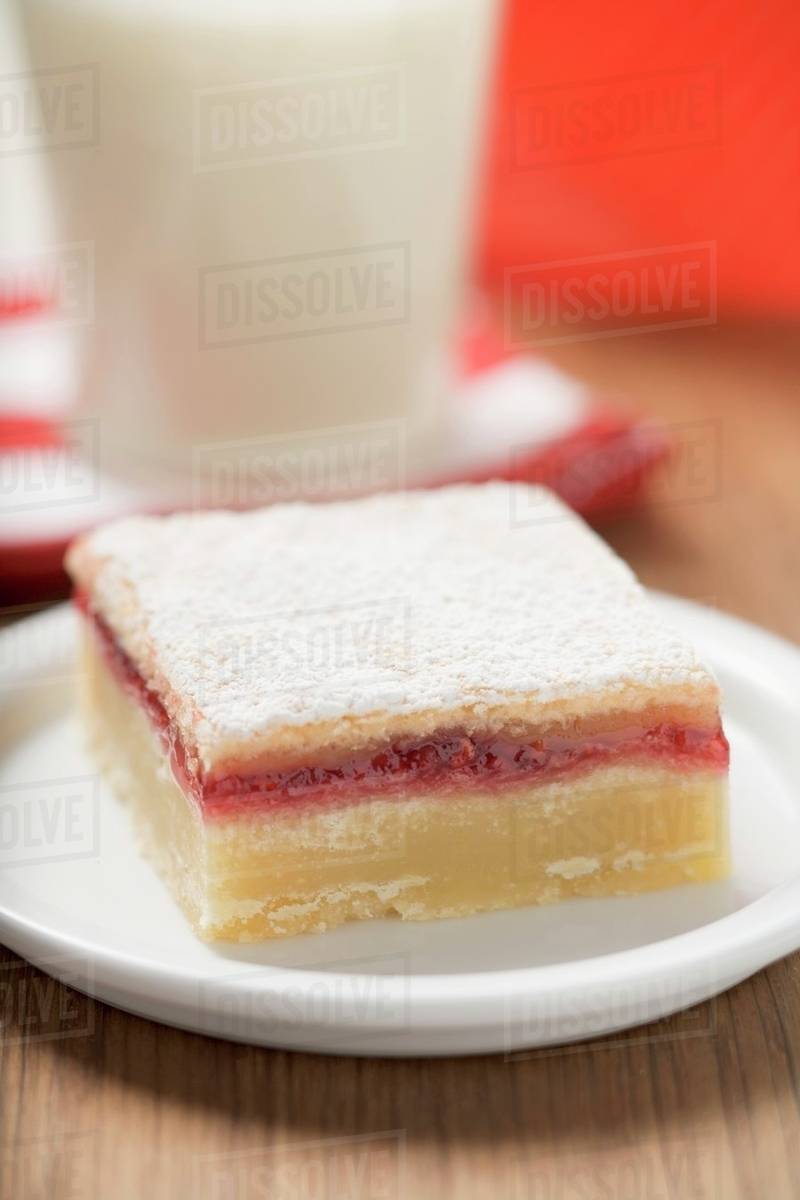Jam slice with icing sugar on plate in front of glass of milk - Royalty ...