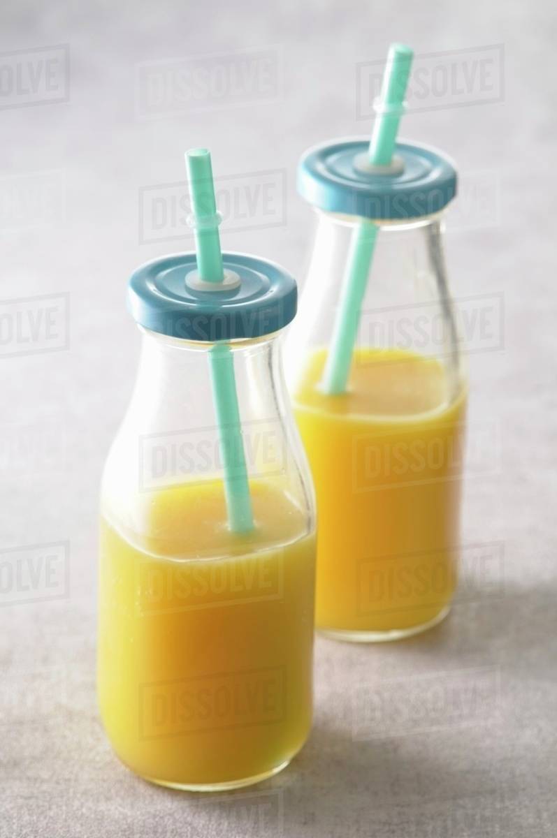 Orange juice in glass bottles with lids and straws Stock Photo Dissolve