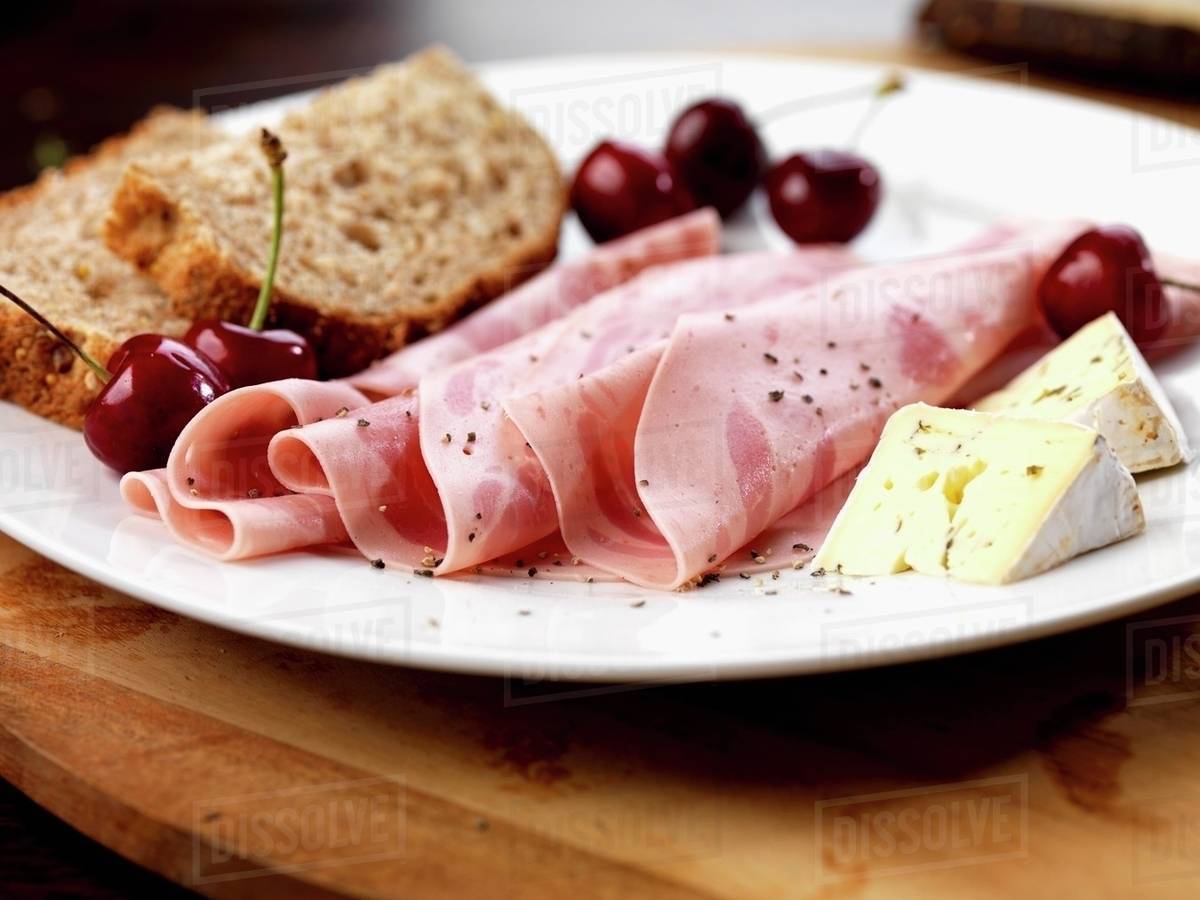 Slices of beer ham, soft cheese, cherries and bread Stock Photo