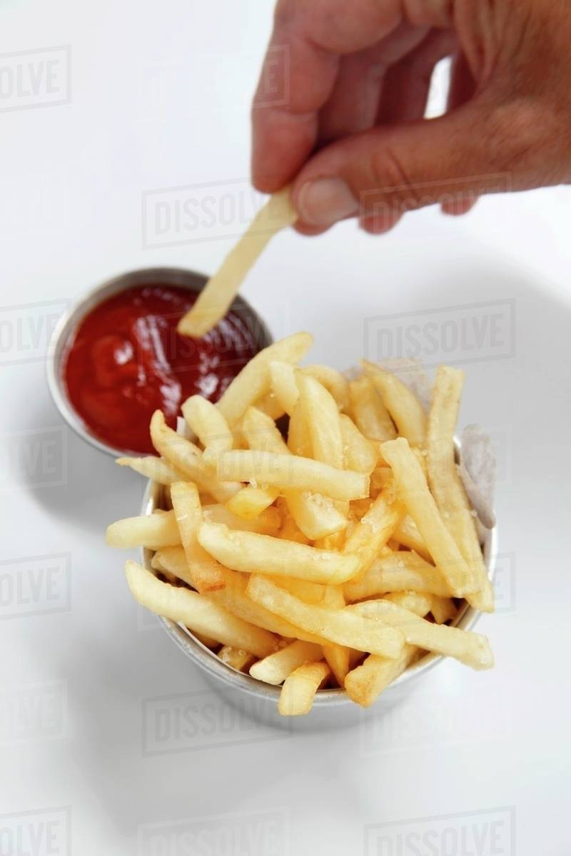 Chips being dipped into ketchup Stock Photo Dissolve