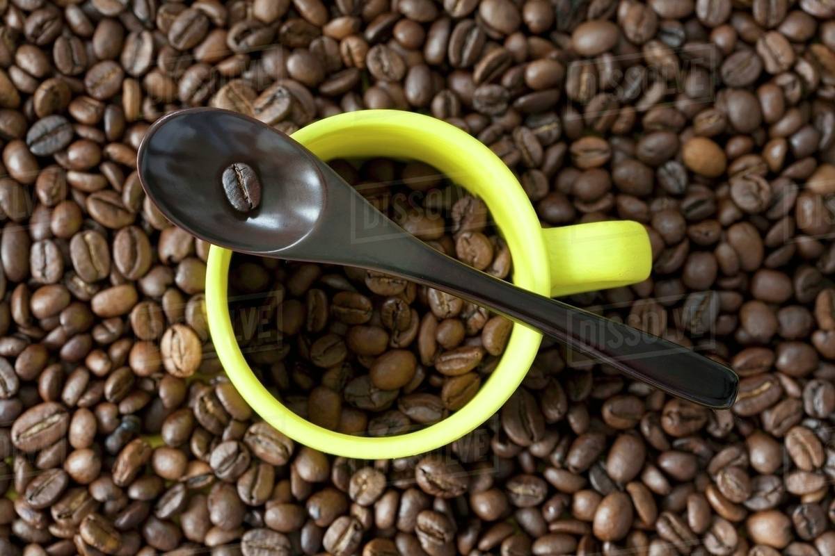 An espresso cup and a spoon on a pile of coffee beans Stock Photo Dissolve