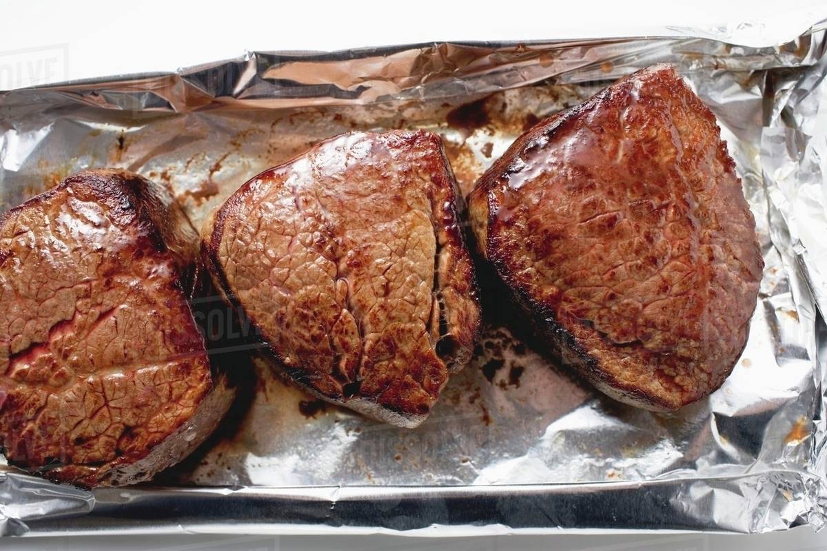 Three fillet steaks on aluminium foil Stock Photo Dissolve