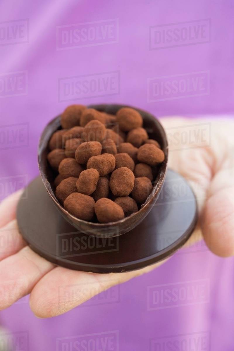 Hand holding half a chocolate egg filled with chocolate truffles
