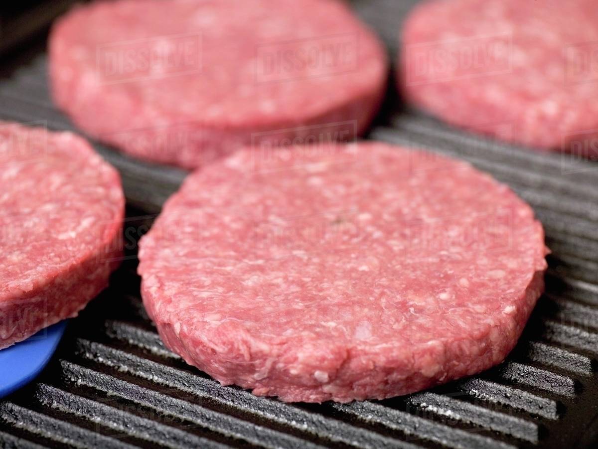 Raw burgers on electric grill Stock Photo Dissolve