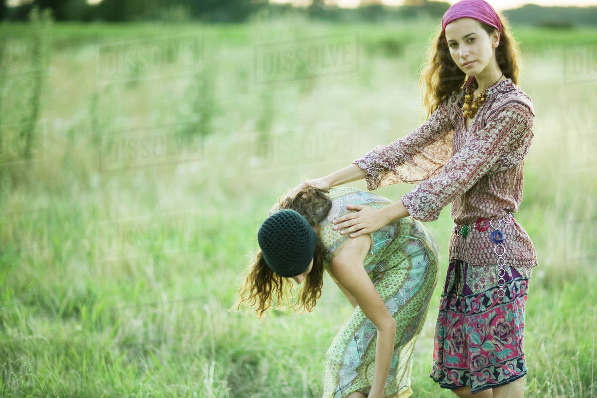 Young women in field, one bending over while the other holds her back
