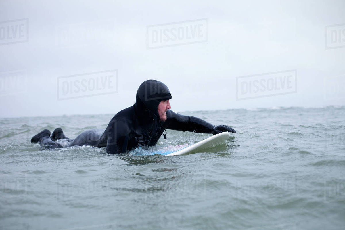 Surfer wearing wetsuit floating with board in wintery sea Stock Photo