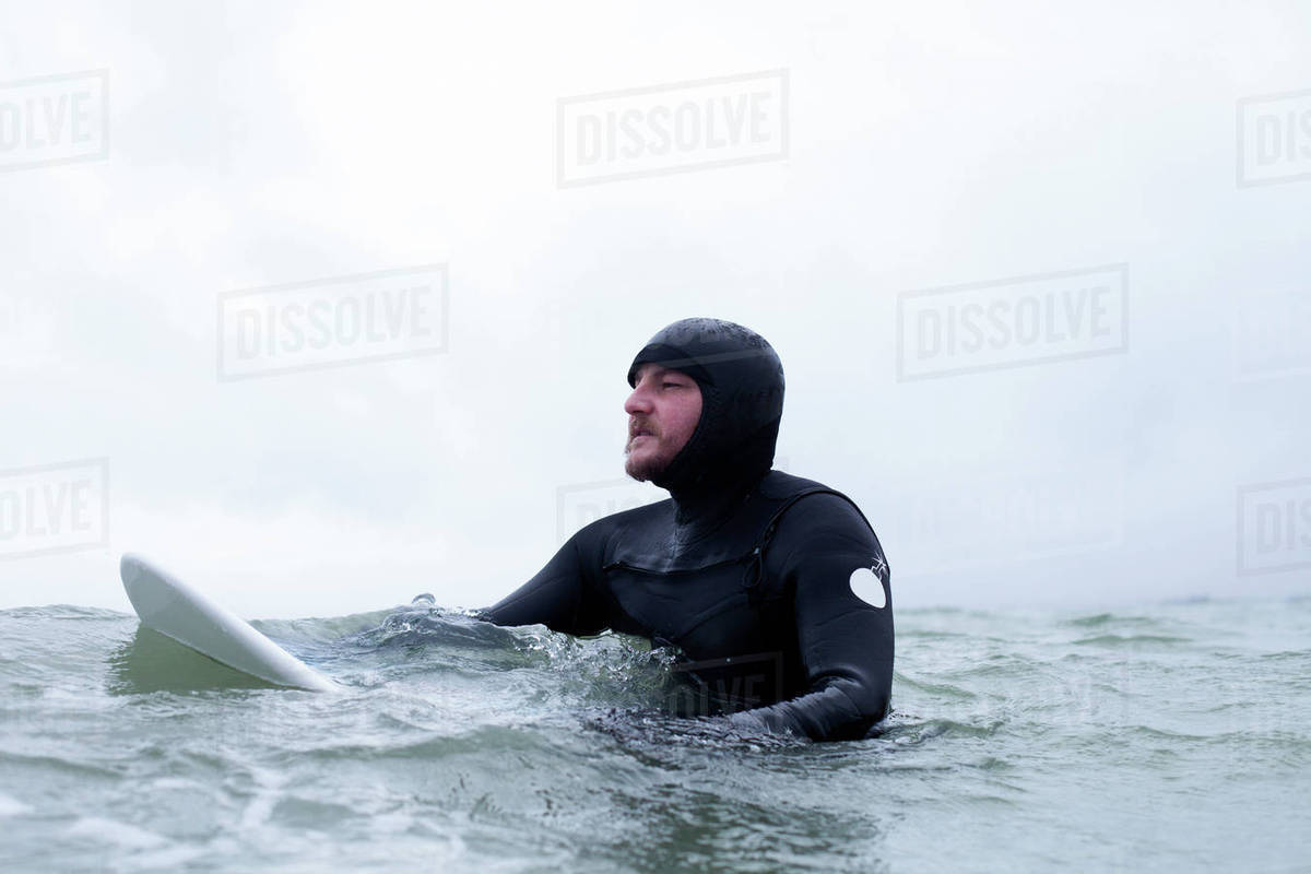 Surfer wearing wetsuit floating with board in wintery sea Stock Photo