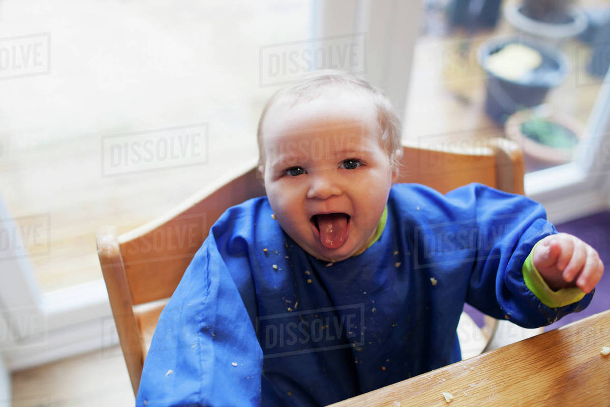 Baby girl sitting in high chair at meal time Stock Photo Dissolve