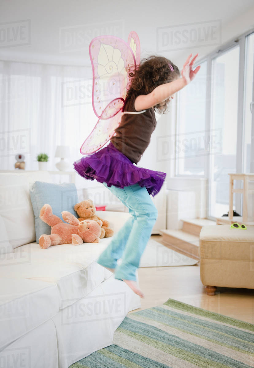 Hispanic girl in fairy wings jumping off couch Royalty-free stock photo