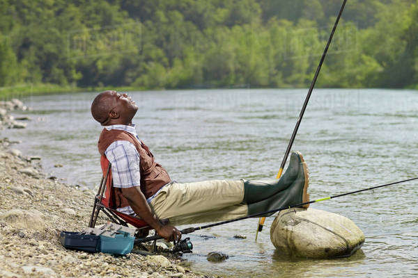 Black man with feet up fishing in stream - Royalty-free Stock Photo ...