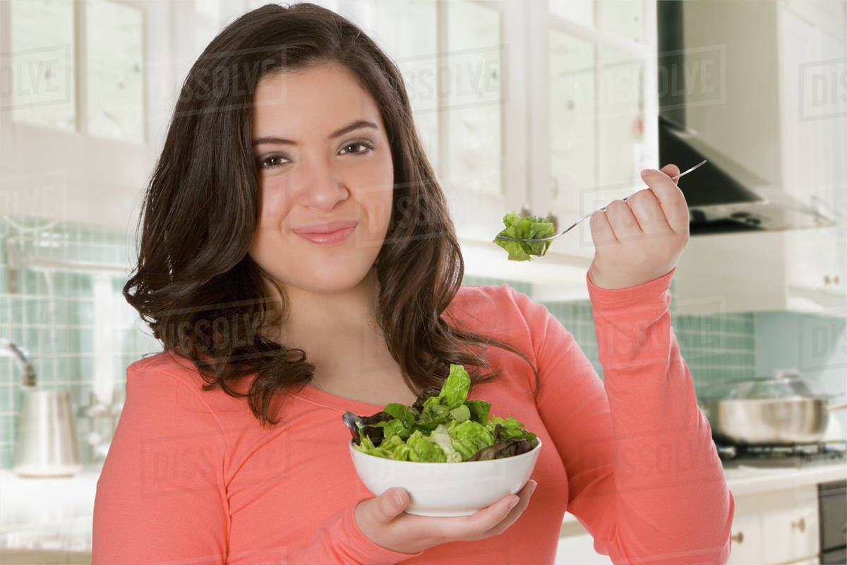 Hispanic teenage girl eating salad in kitchen Stock Photo Dissolve