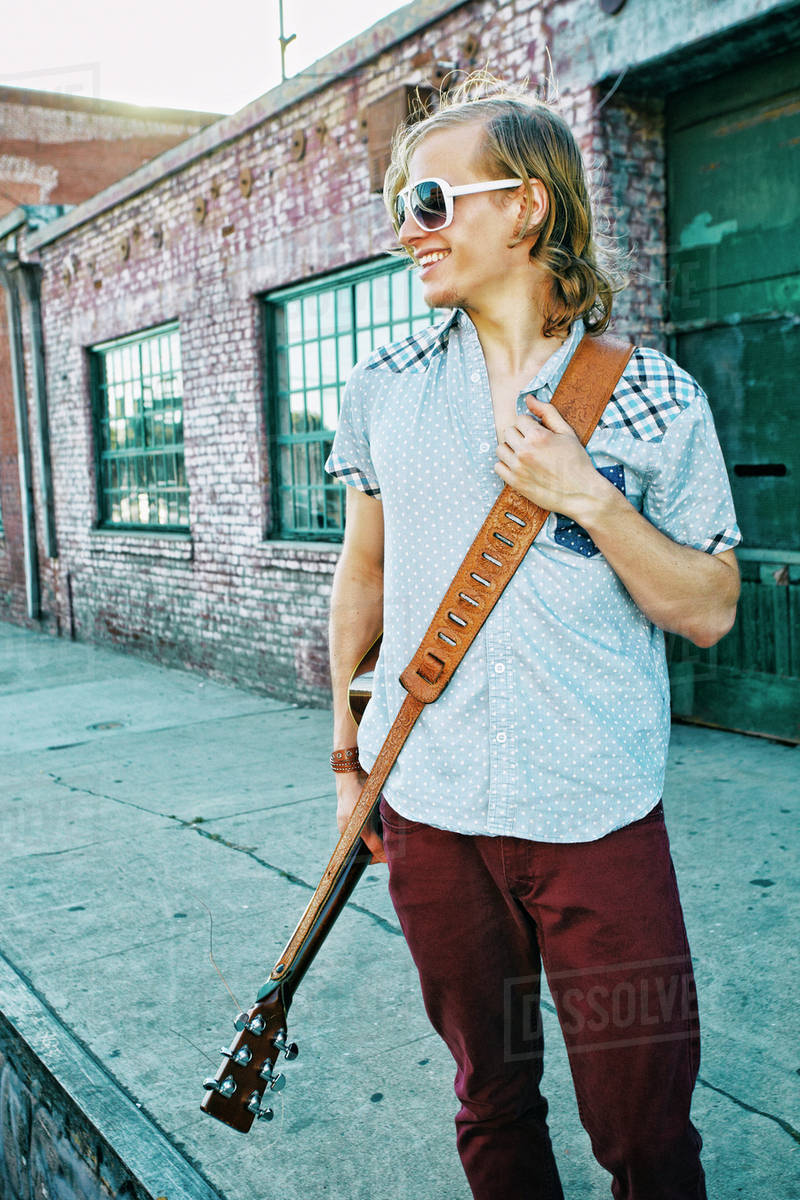 Caucasian man carrying guitar outdoors Stock Photo Dissolve