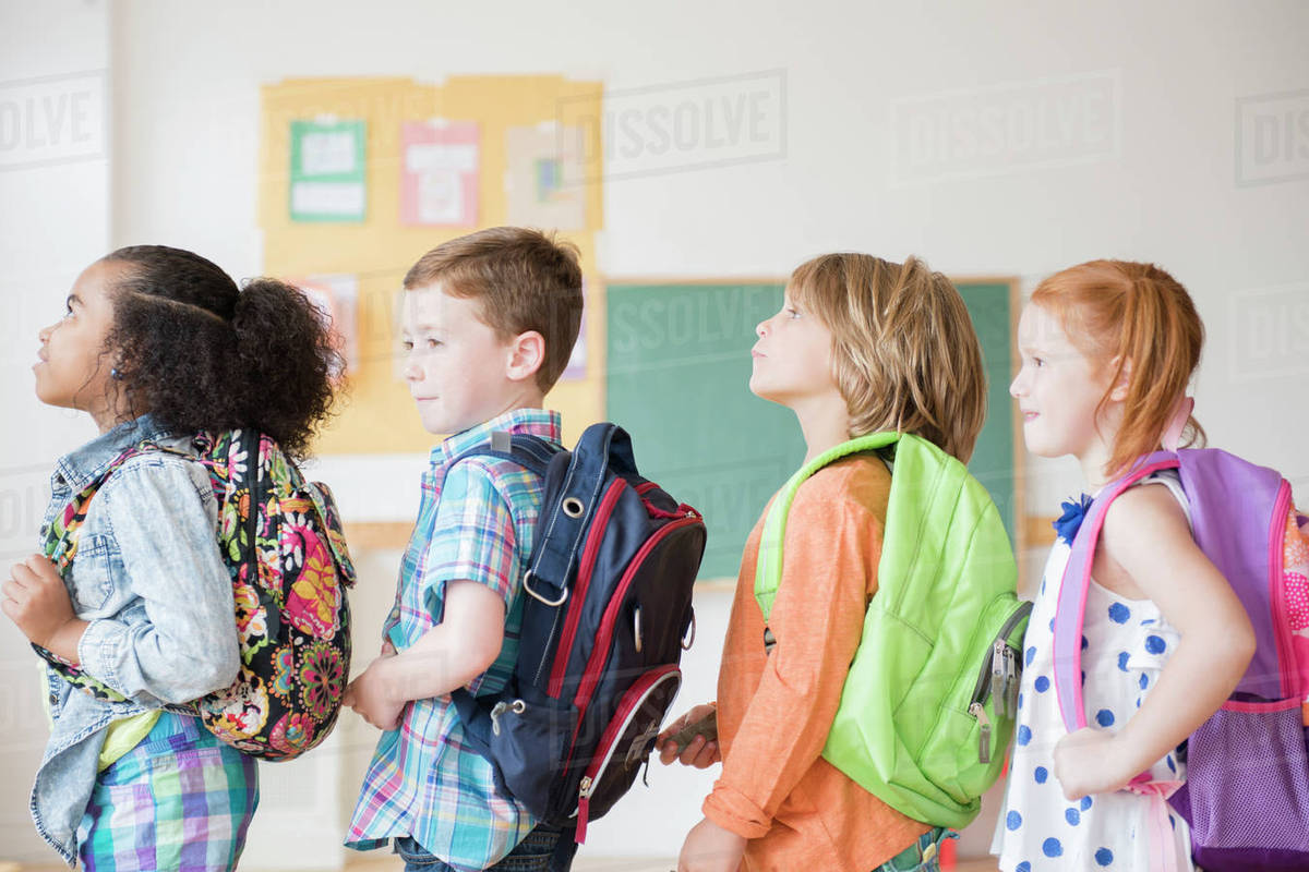 Students wearing backpacks in classroom Stock Photo Dissolve