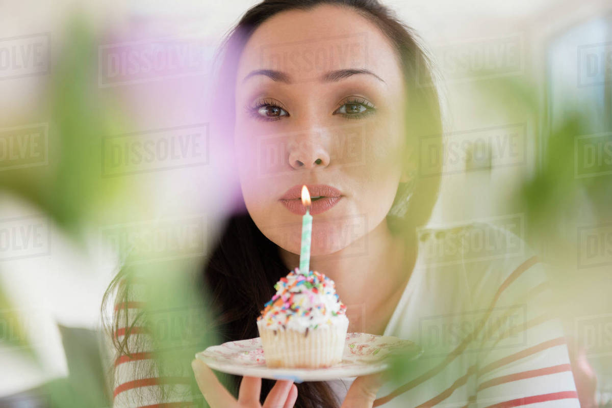 Woman blowing out birthday candle on cupcake Stock Photo Dissolve