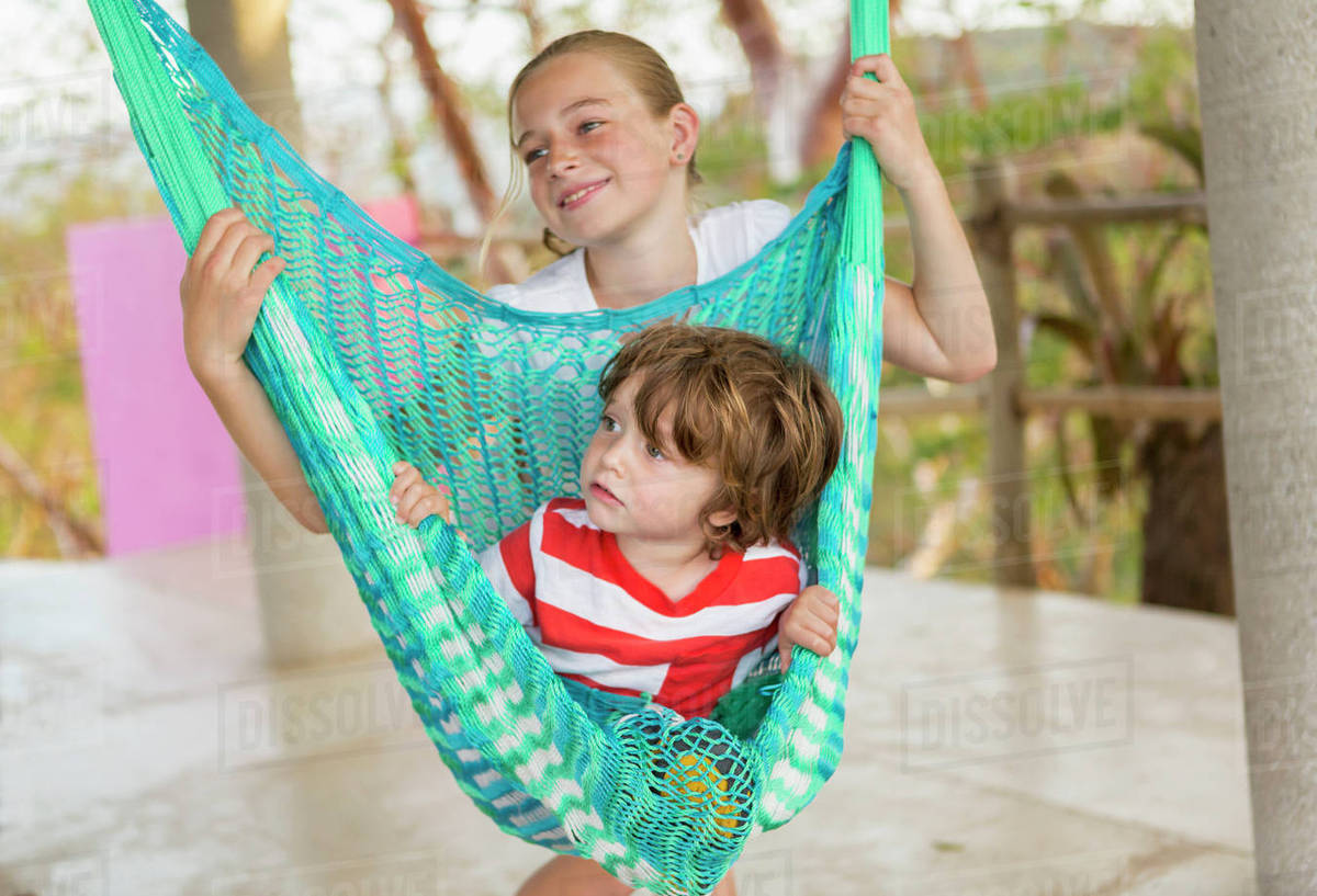 Caucasian boy sitting in hammock held by sister Stock Photo Dissolve