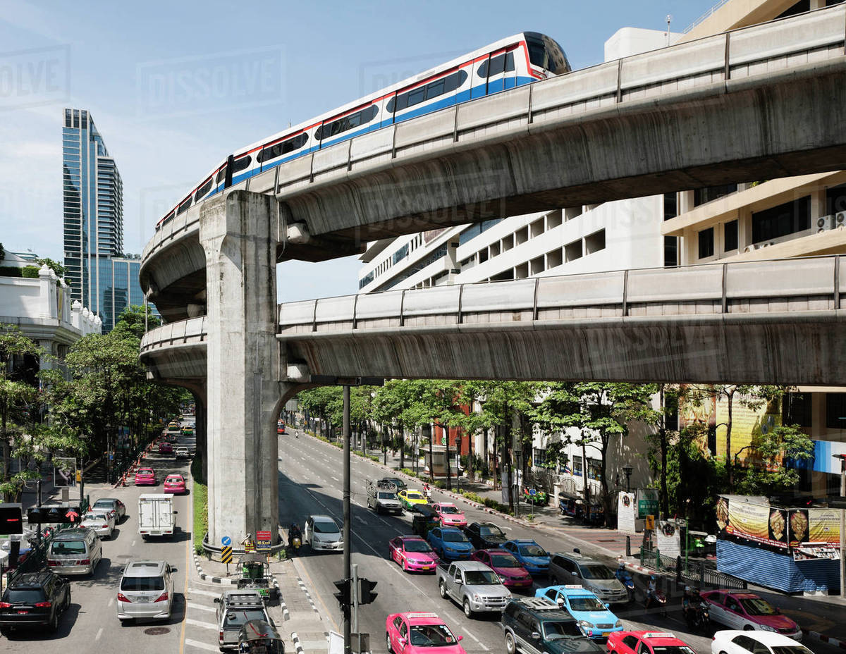 A mass transit train on an elevated track passes modern building