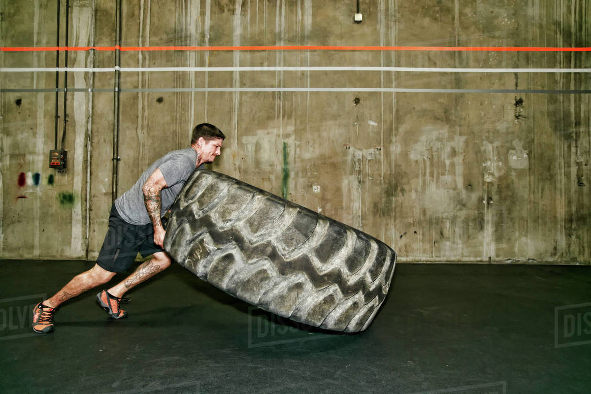 Caucasian man lifting large tire in gym Stock Photo Dissolve