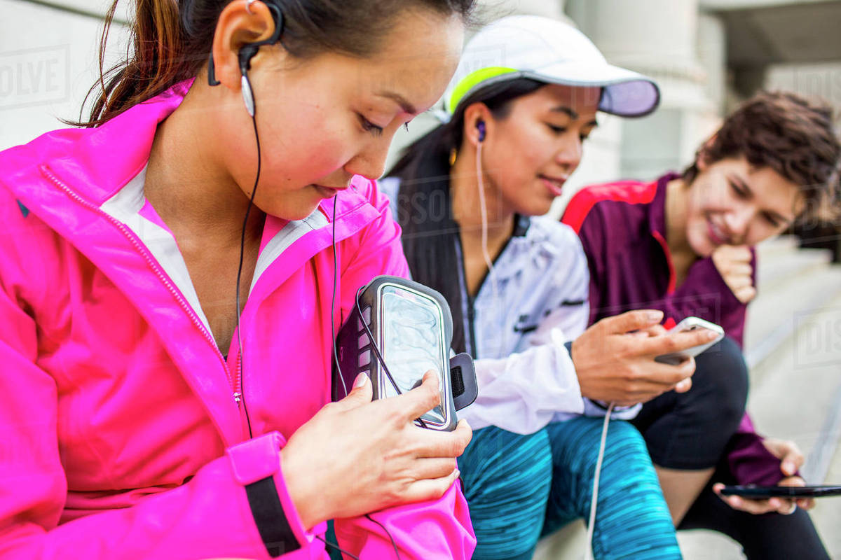 Runners using cell phones and earbud on city sidewalk Stock Photo