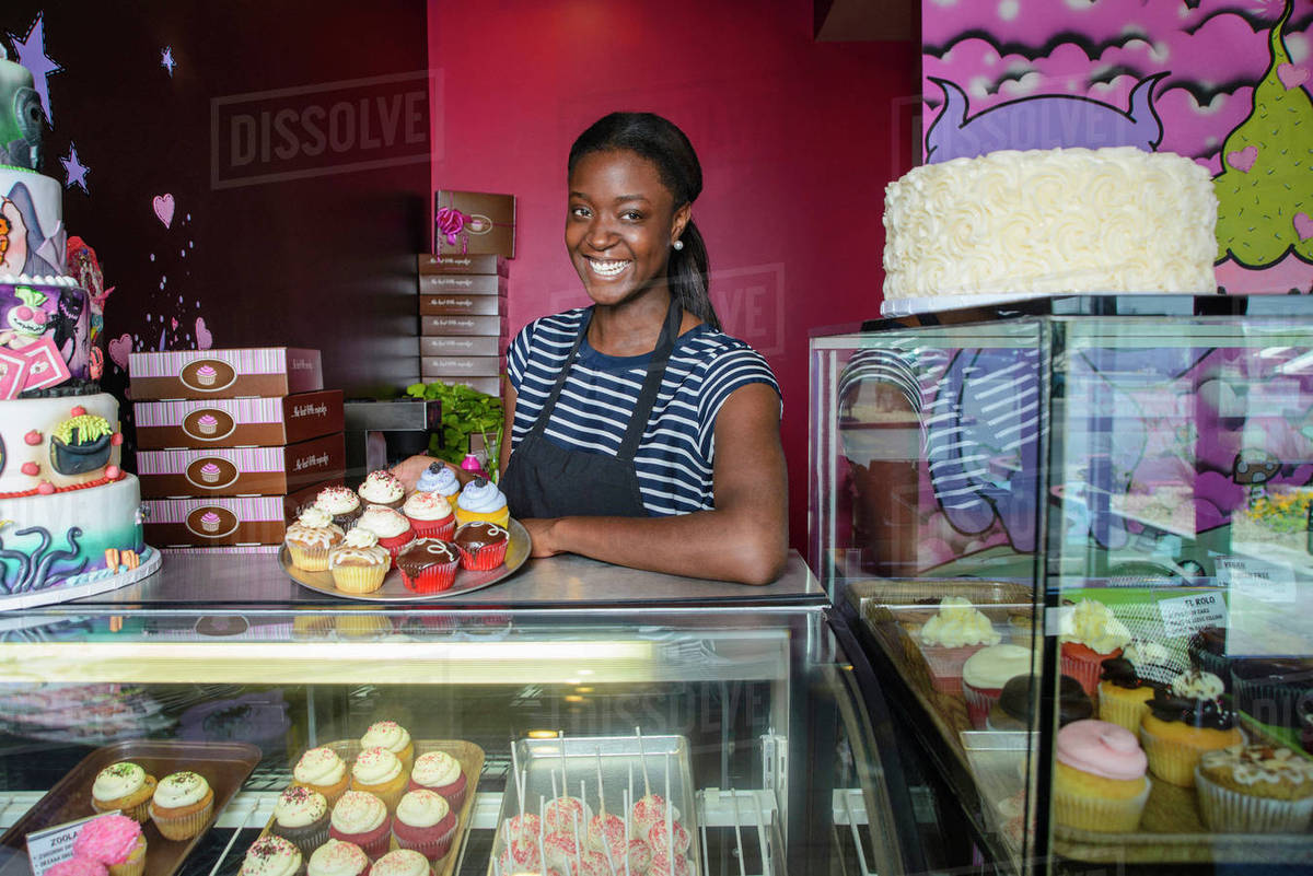 Black business owner showing cupcakes at bakery display case Stock