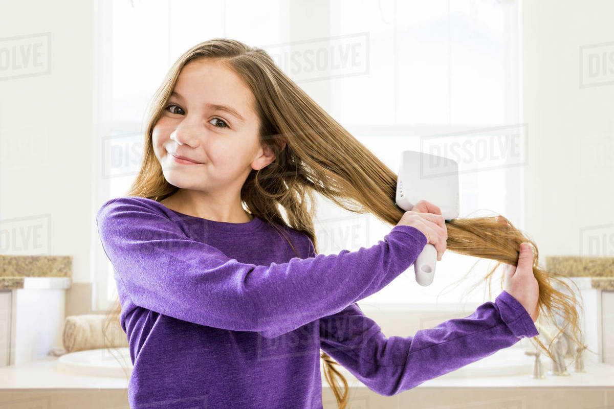 Caucasian girl brushing hair in bathroom Stock Photo Dissolve