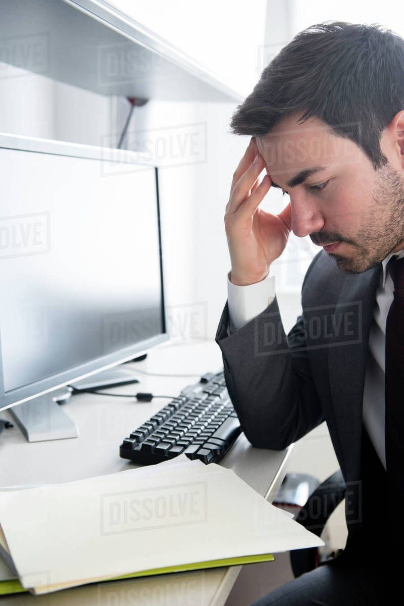 Businessman with headache at office desk Stock Photo Dissolve