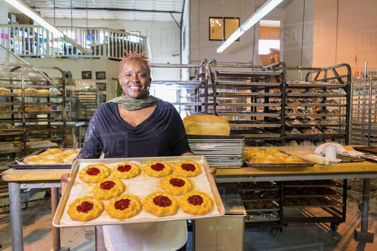 Black baker holding tray of pastries in bakery kitchen Stock Photo