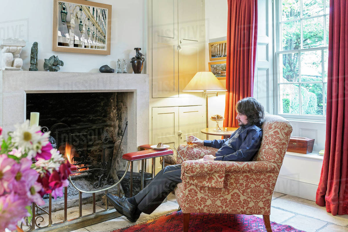 Man sitting in armchair near fireplace drinking cocktail Stock Photo