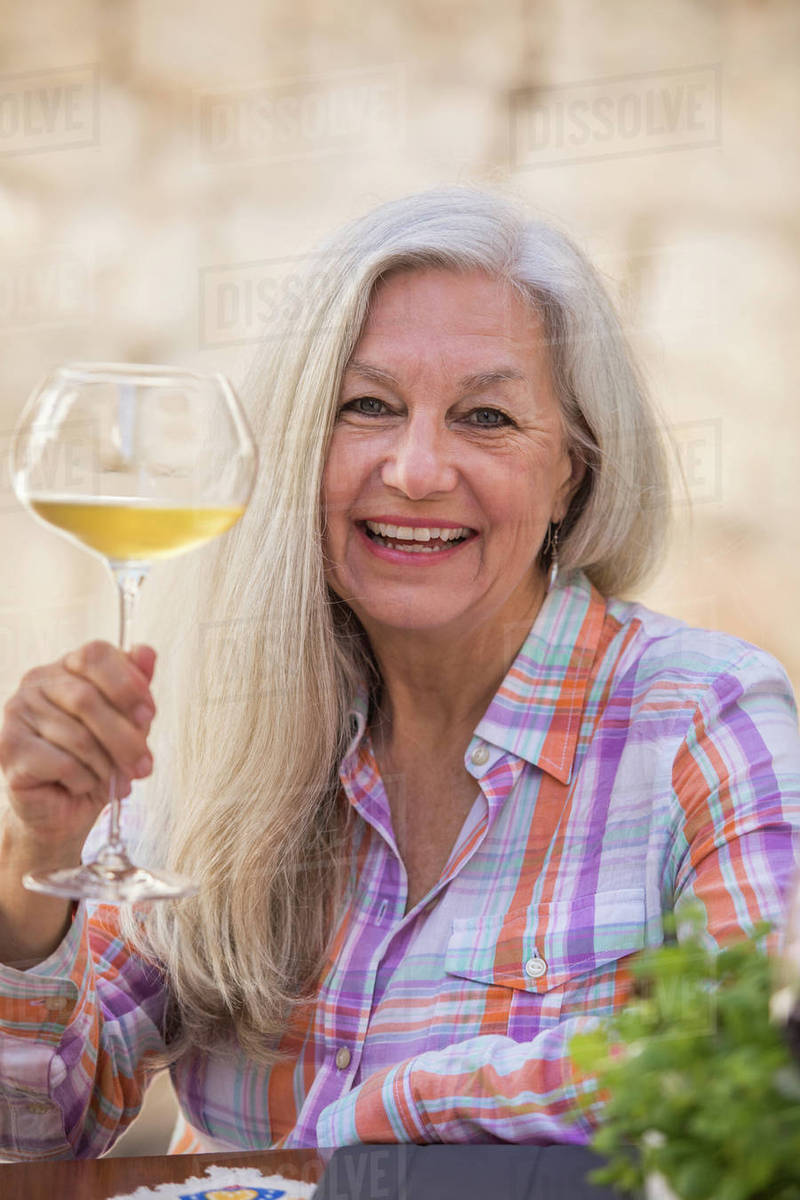 Smiling older Caucasian woman holding white wine Stock Photo Dissolve
