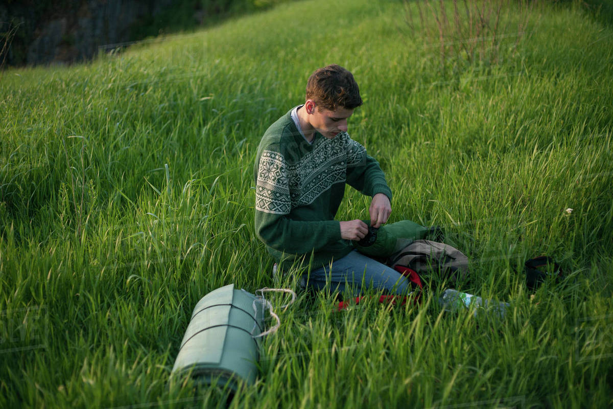 Caucasian hiker kneeling in grass Stock Photo Dissolve