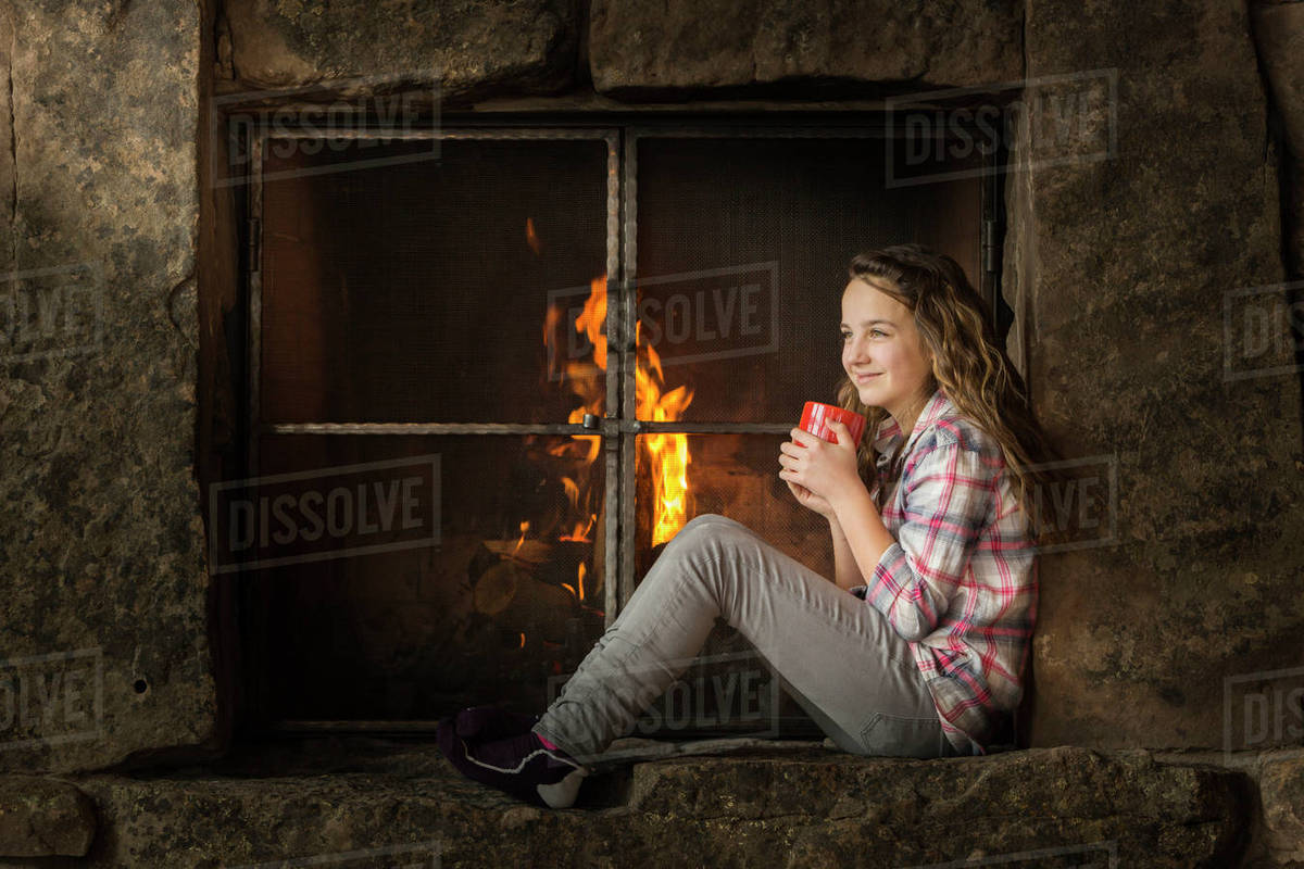 Smiling Caucasian girl sitting near fireplace Stock Photo Dissolve