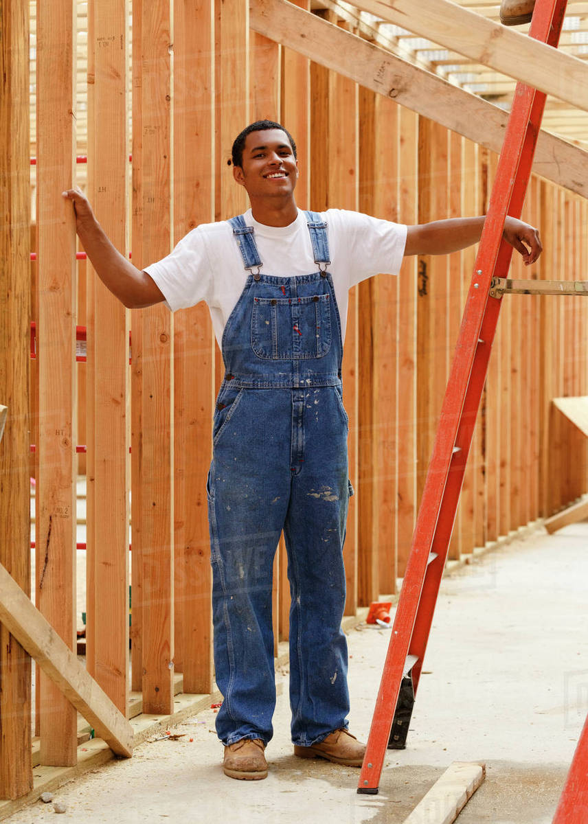 Portrait of smiling mixed race man leaning on ladder at construction ...