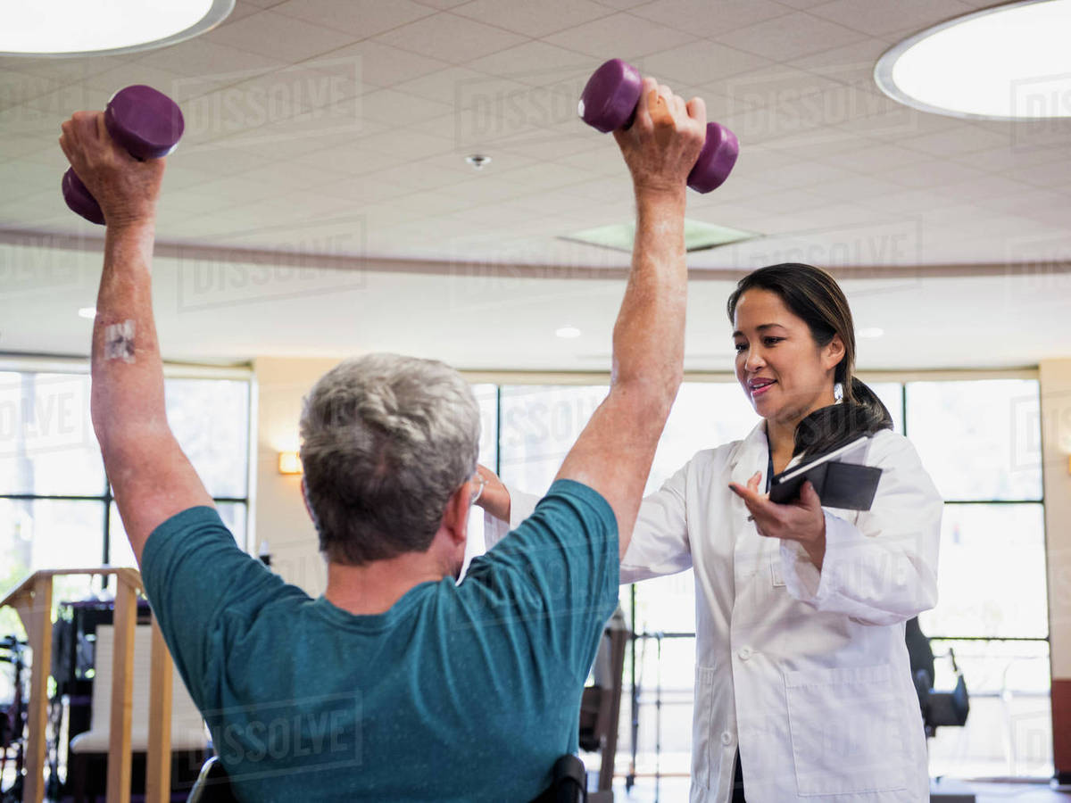 Physical therapist helping man lifting weights Stock Photo Dissolve