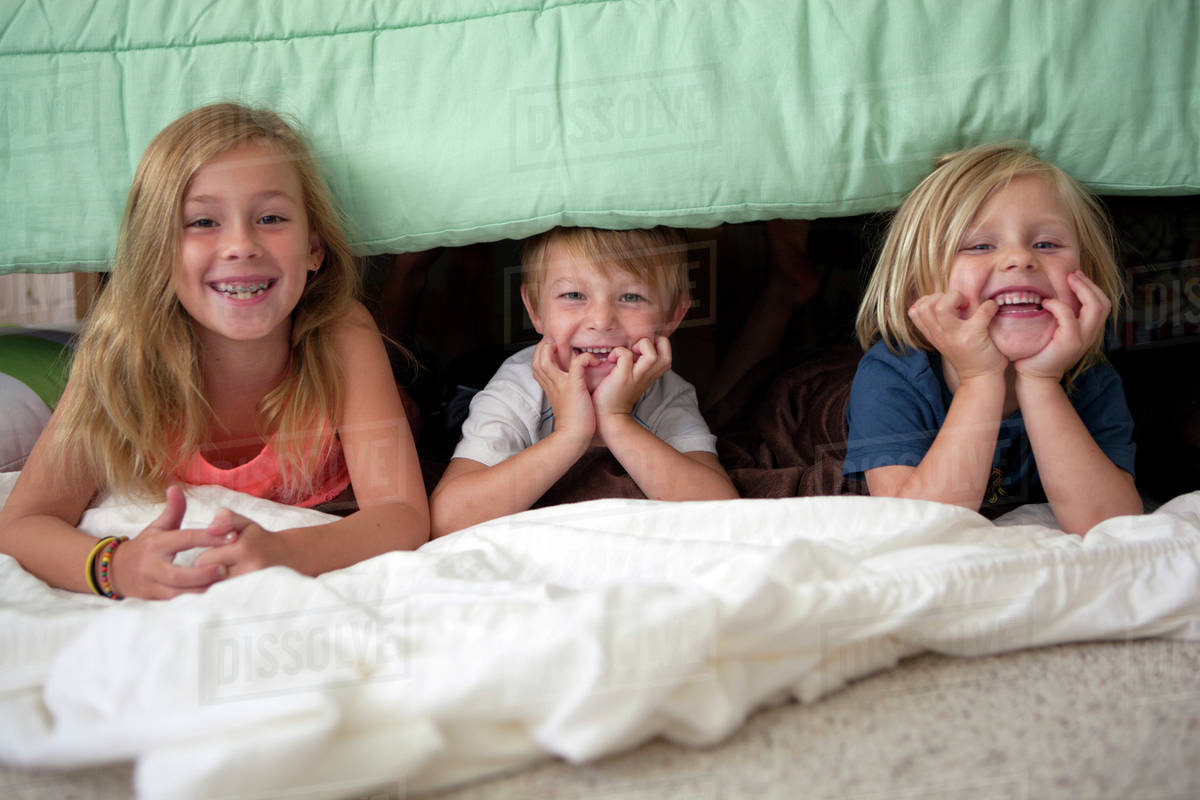 Caucasian children laying under bed Stock Photo Dissolve