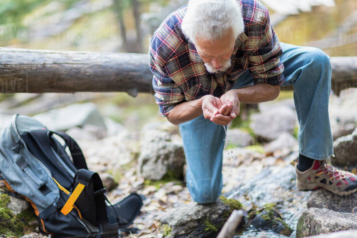 Caucasian hiker drinking water from creek in forest Stock Photo