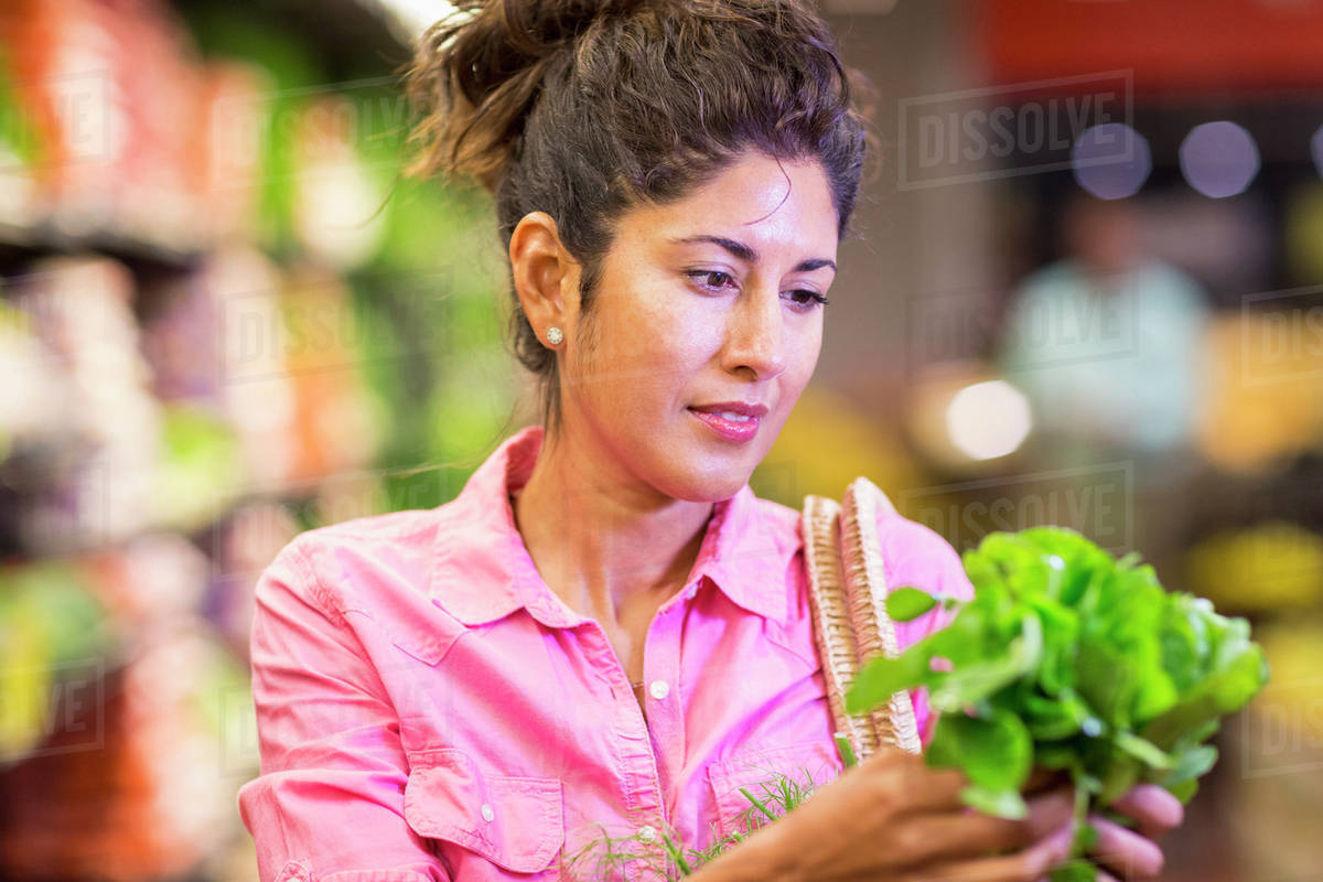 Hispanic woman examining produce at grocery store Stock Photo Dissolve