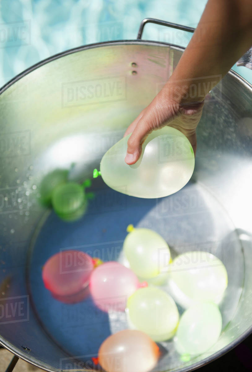 Hispanic girl picking water balloon out of bucket Stock Photo Dissolve